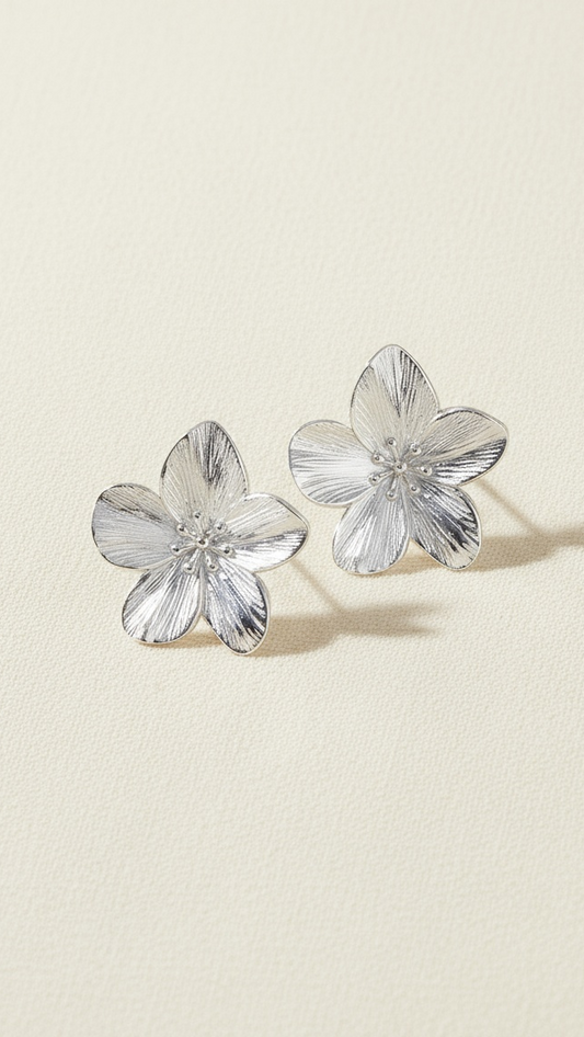 Flower-shaped silver earrings on a beige background